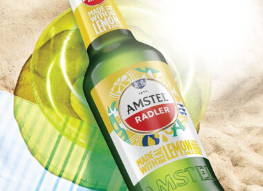 Amstel Radler's new packaging design done by Berge Farrell design. The newly designed Amster Radler is on a beach-themed background in this image, above a towel, sand and lilo.